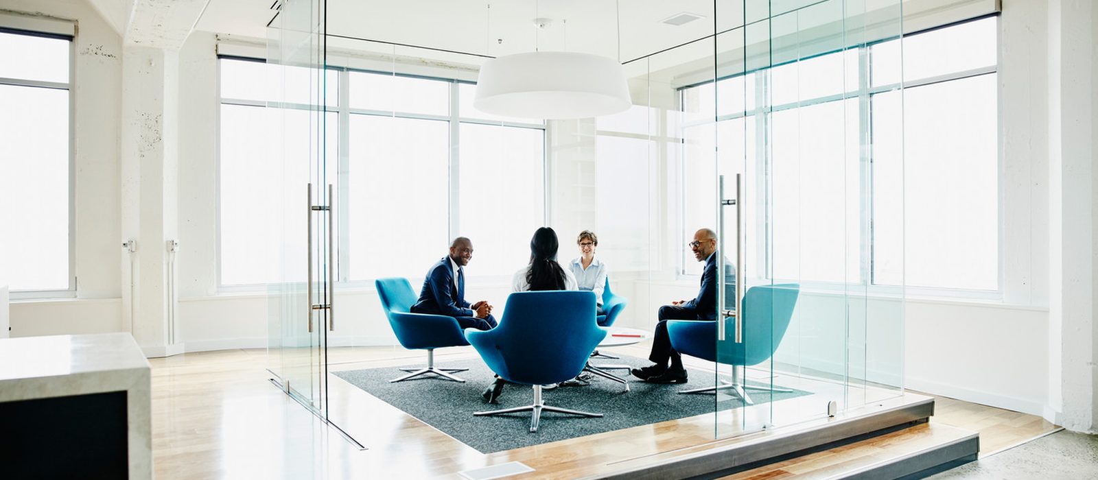 A leadership team meeting in a glass-walled room, seen from outside.